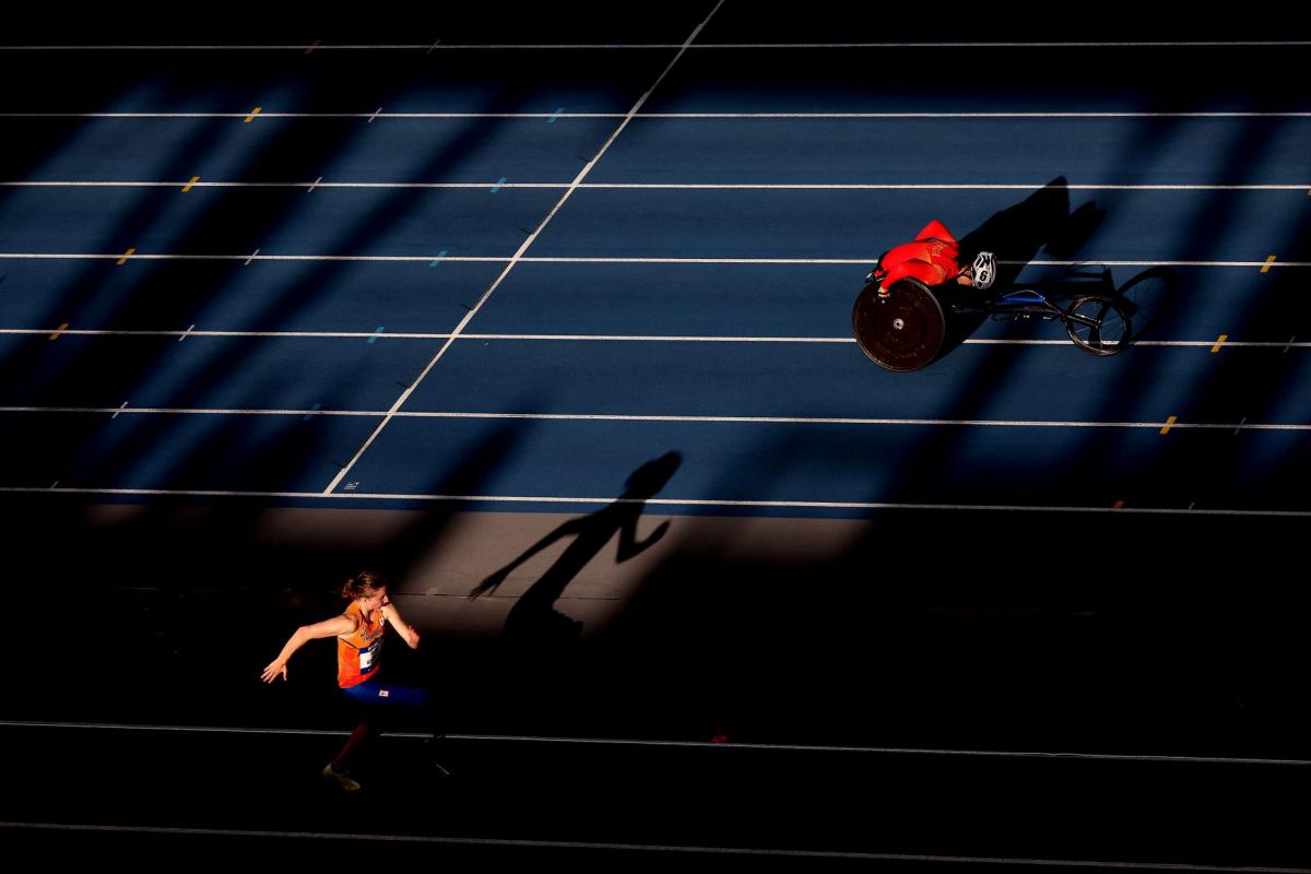 A female athlete with prosthetic legs jumping next to a wheelchair racer in the track